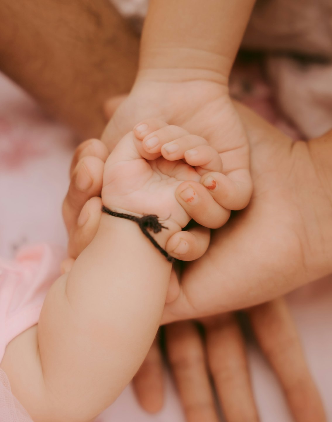 Een volwassen hand houdt twee babyhandjes samen vast.