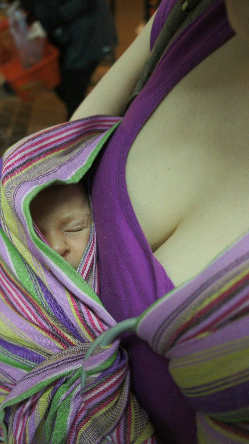 Een baby slaapt vredig in een kleurrijke gestreepte stoffen draagzak.