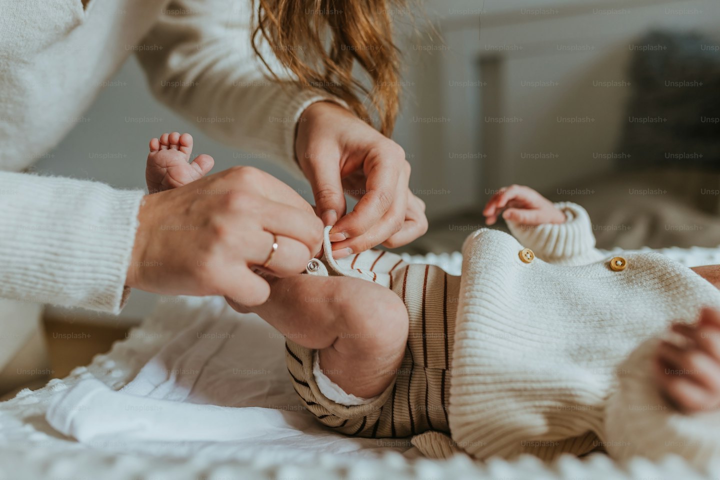Handen sluiten drukknoopjes op een gestreepte babyromper.