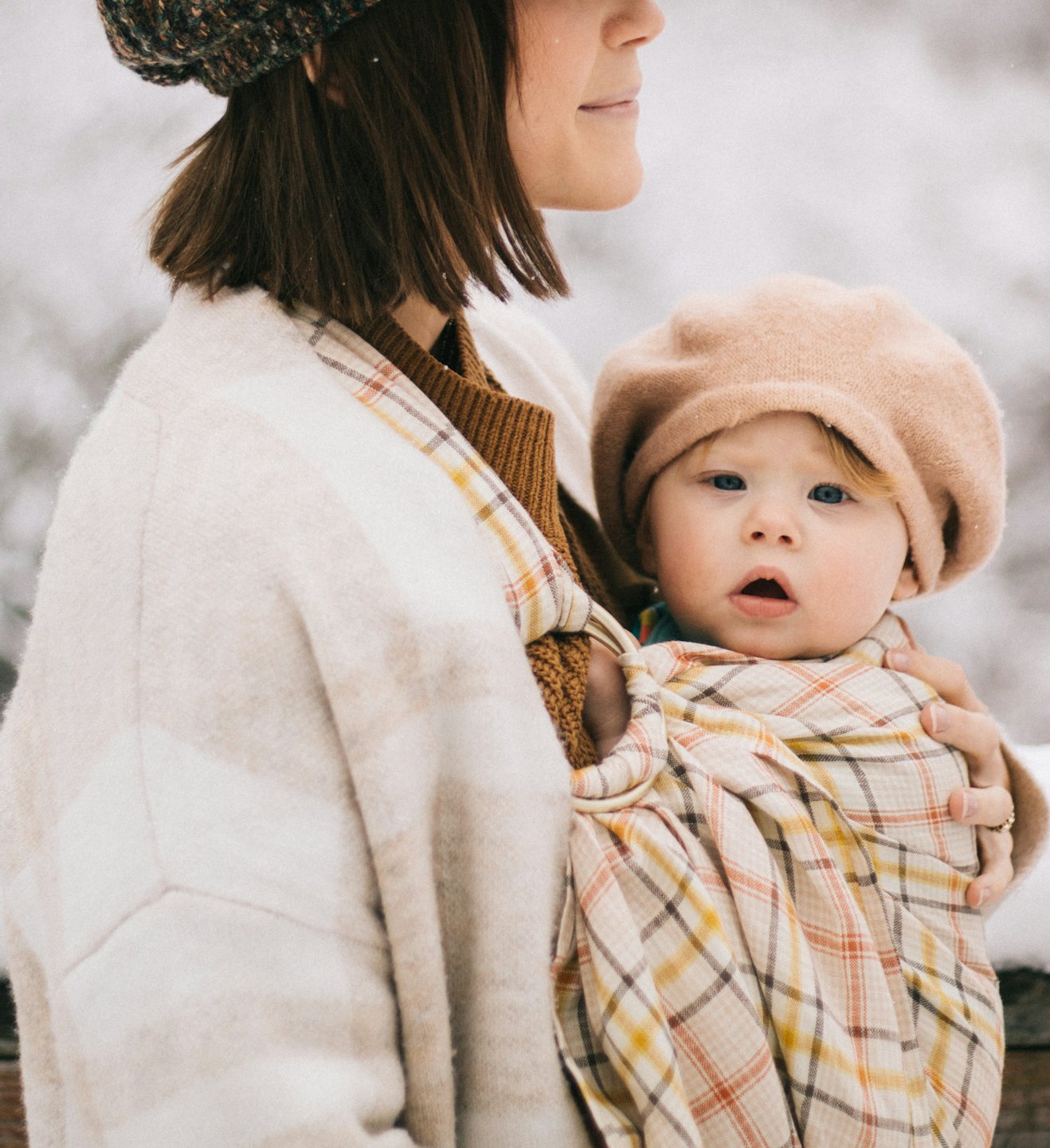 Ouder draagt baby in een geruite ringsjaal buiten in de sneeuw.